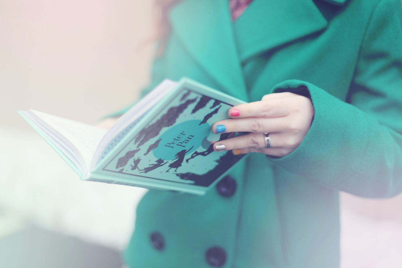 Kobieta w turkusowym płaszczu trzyma otwartą książkę.